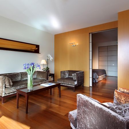 فندق يوروستارز غراند مارينا جي إل برشلونة المظهر الخارجي الصورة The photo shows a modern living room with a warm and inviting atmosphere. It features two armchairs and a sofa, all in a plush, dark fabric. A coffee table sits in the center, with a vase of fresh flowers adding a pop of color. The room has hardwood 