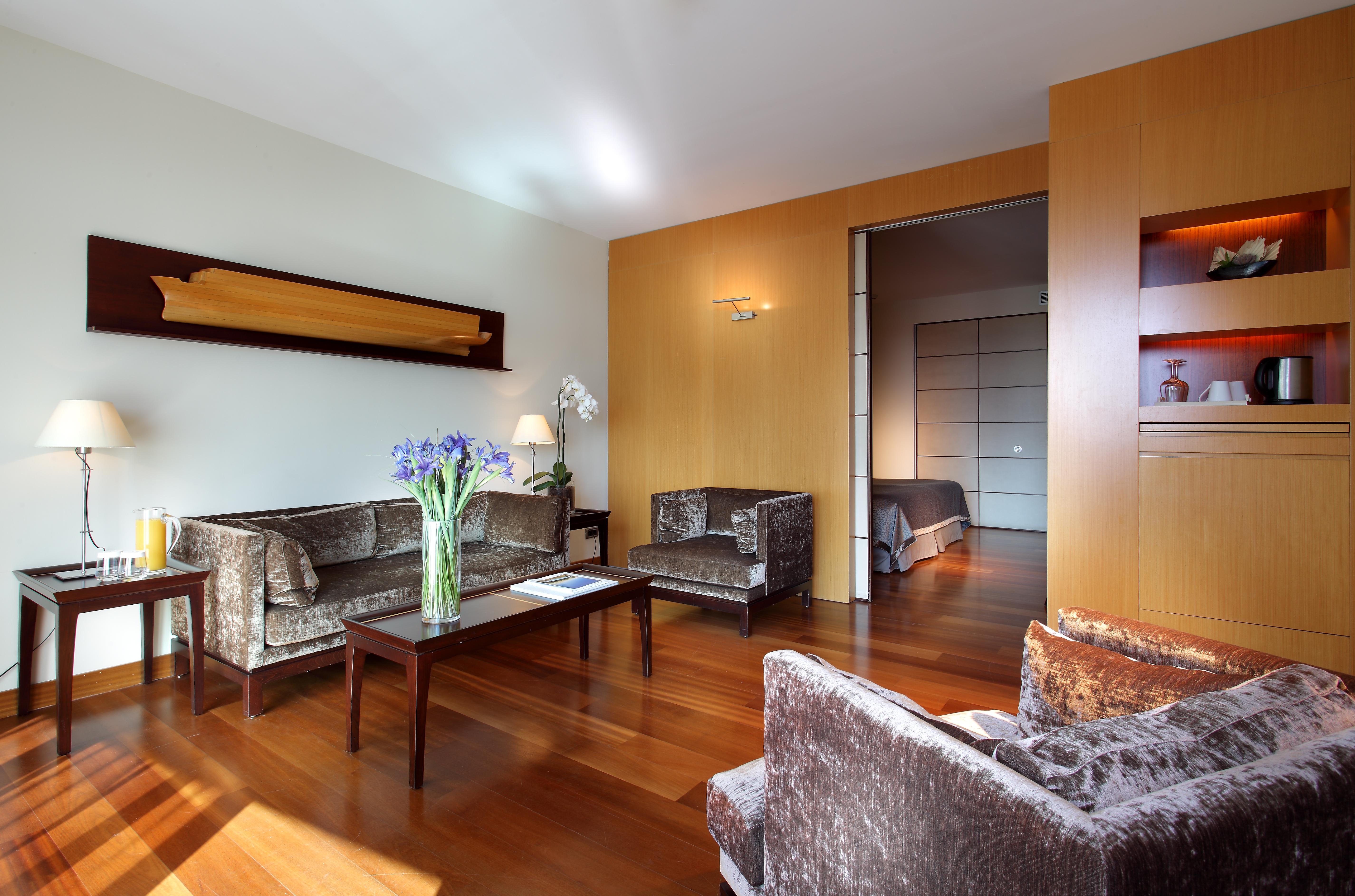 فندق يوروستارز غراند مارينا جي إل برشلونة المظهر الخارجي الصورة The photo shows a modern living room with a warm and inviting atmosphere. It features two armchairs and a sofa, all in a plush, dark fabric. A coffee table sits in the center, with a vase of fresh flowers adding a pop of color. The room has hardwood 