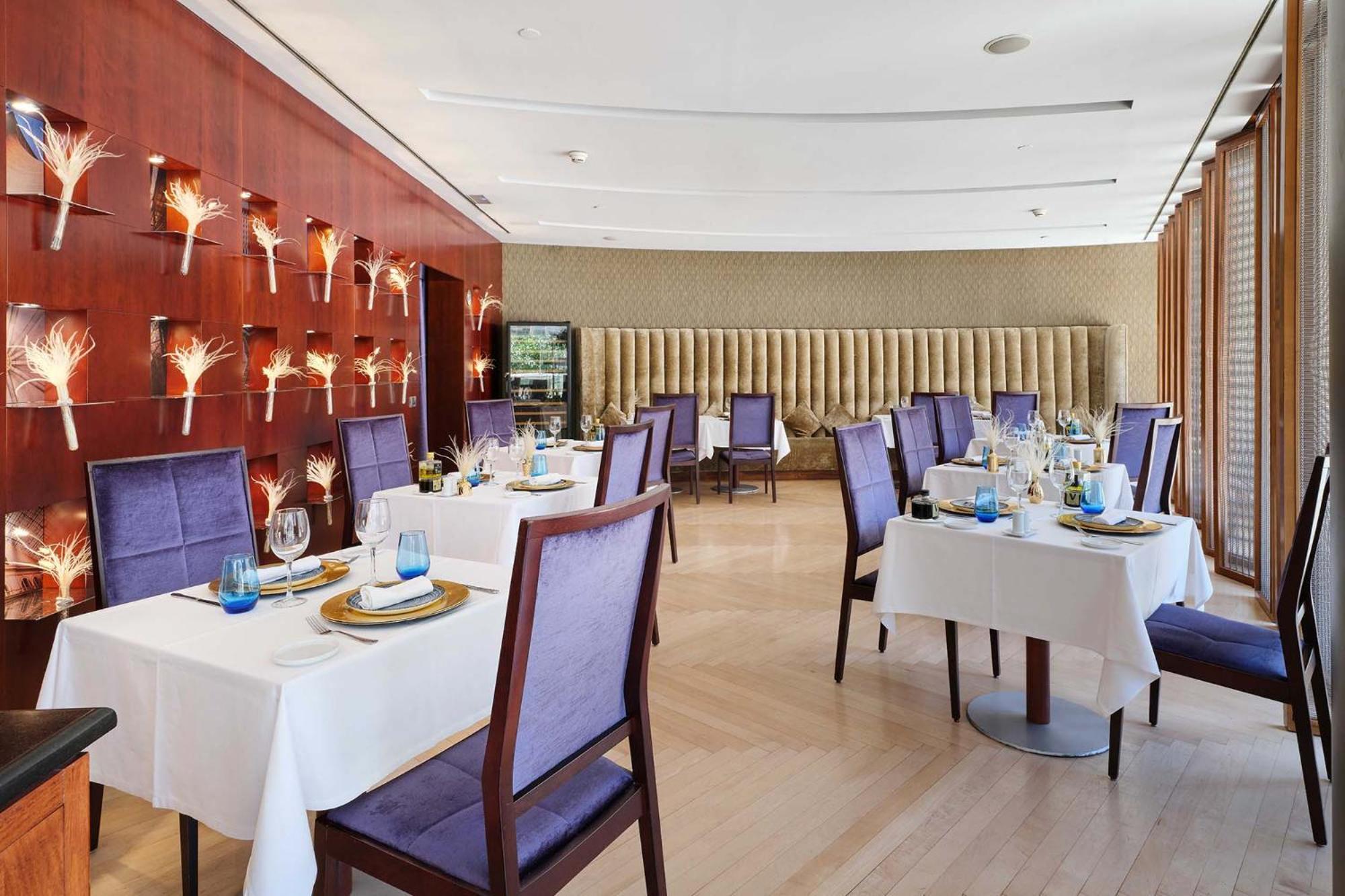 فندق يوروستارز غراند مارينا جي إل برشلونة المظهر الخارجي الصورة The photo shows an elegant dining room in a restaurant. There are several tables set with white tablecloths, each adorned with plates, glasses, and decorative items. The chairs have a purple upholstery, adding a touch of color to the space. 

The wal