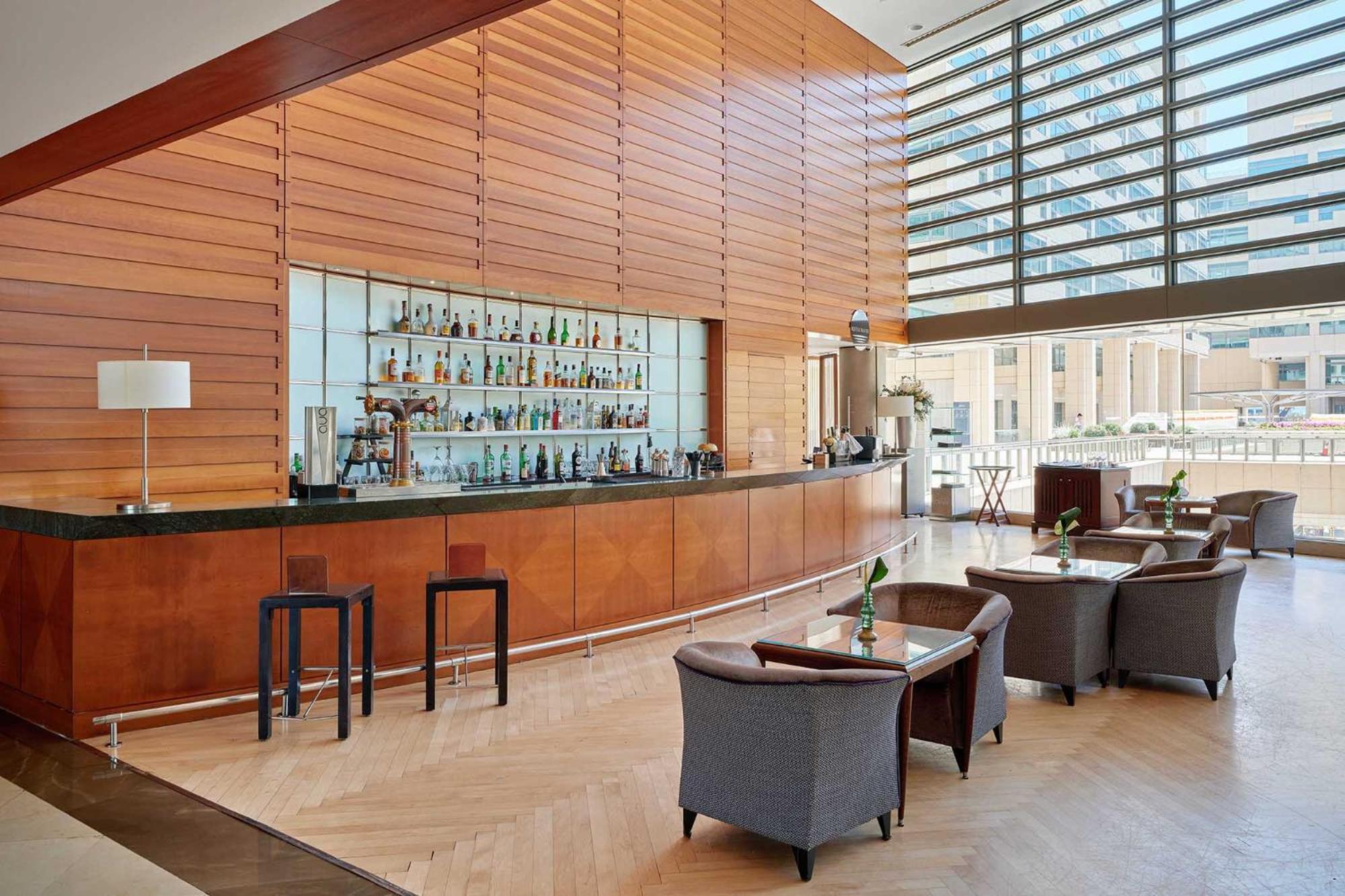 فندق يوروستارز غراند مارينا جي إل برشلونة المظهر الخارجي الصورة The photo shows a modern bar area with a sleek, minimalist design. There is a long, polished bar countertop behind which various bottles of drinks are displayed. The walls feature wooden paneling that creates a warm ambiance, and large windows allow 
